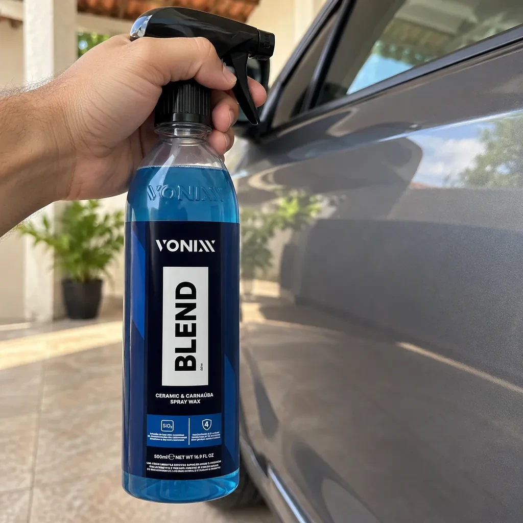 Mão segurando o frasco azul da Vonixx Blend com gatilho, ao lado da porta de um carro cinza estacionado numa garagem com piso de cerâmica